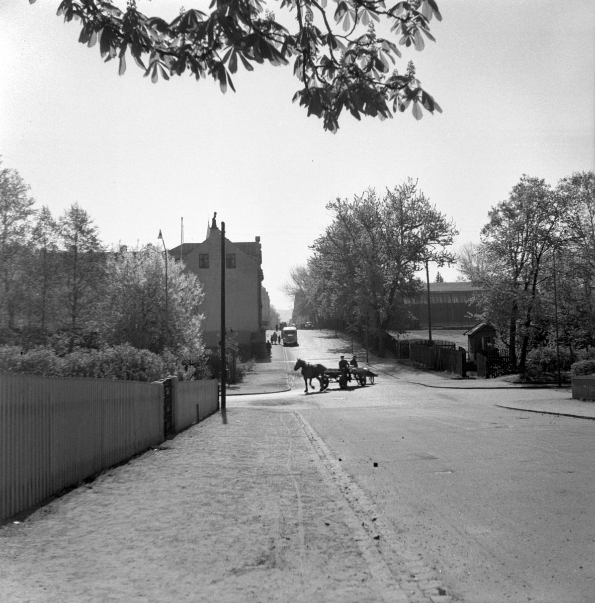 Gatukorsningen Brunnsgatan-Junegatan i Jönköping. Mitt i korsningen två män med häst och vagn. Längre bort på Brunnsgatan syns järnvägsspår.
