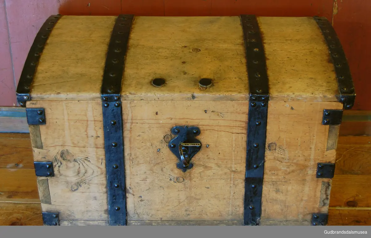 Kiste av furu, naglet med hjemmesmidd jernbeslag på lokk, vegg og hjørner. Oval jernring til håndtak på hver side. Smidd nøkkel. 