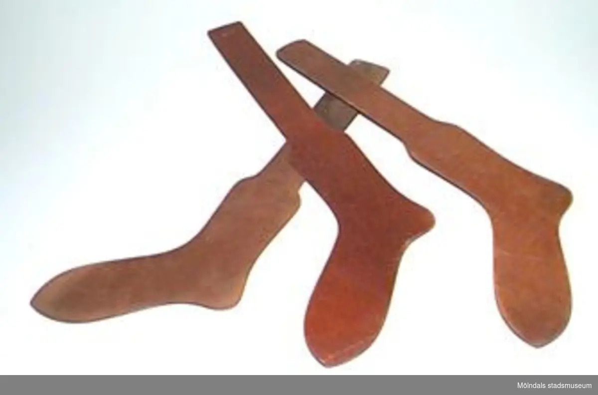 Tre s k strumppressformar. De stacks in i nytillverkade ankelstrumpor för att det skulle gå lätt att pressa strumpan. En pressform (brun) är för storlek 10 1/2, två (en brun och en vinröd) är för strumpstorlek 11 1/2, dvs herrstorlekar. De är från Viktor Samuelsons fabrik "Strumpan".
