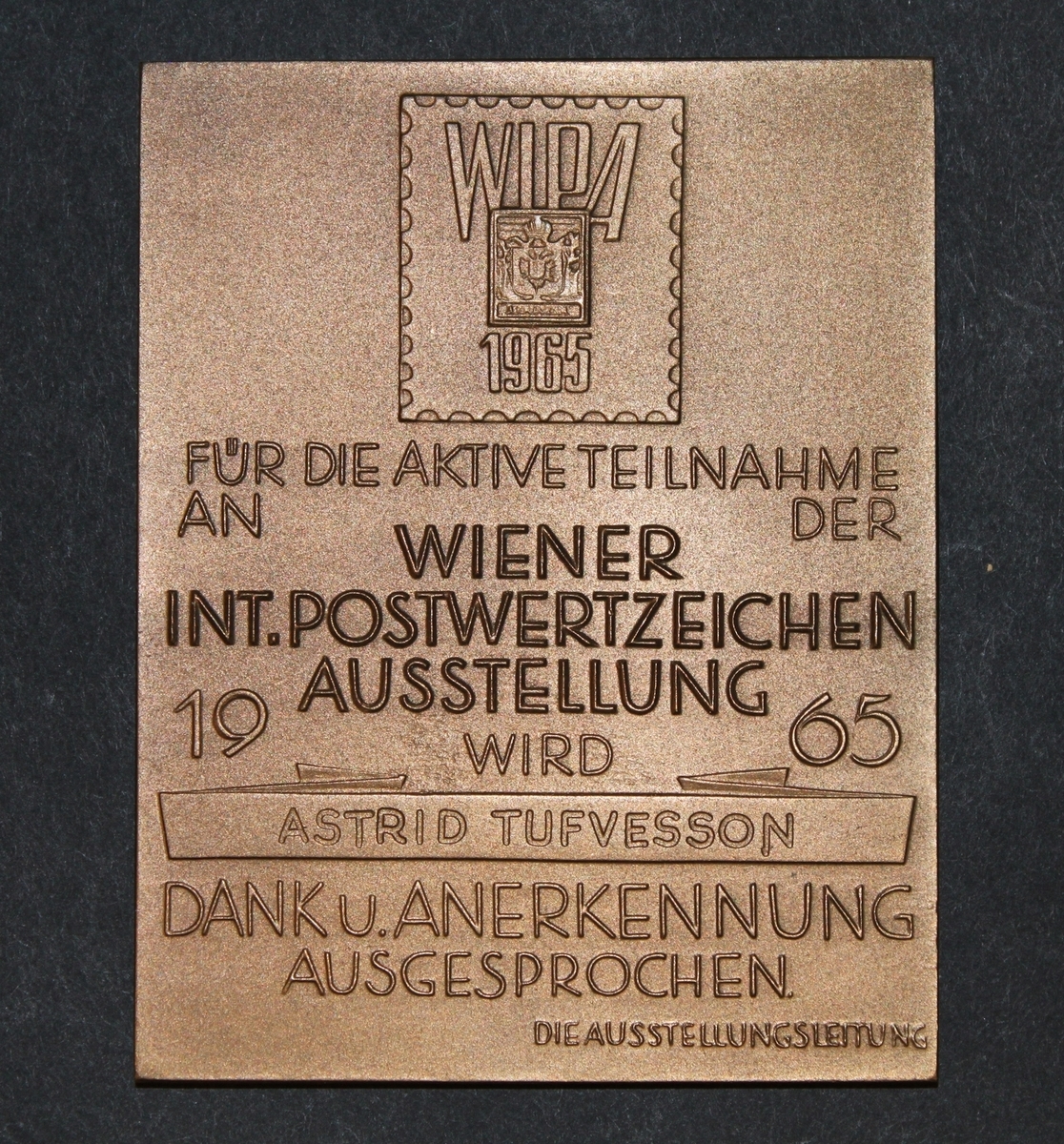 Plakett, rektangulär. Plaketten visar inom en liten ram en
bild av Österrikes första frimärke och texten: WIPA 1965, därunder
står texten: FÜR DIE AKTIVE TEILNAHME AN DER WIENER INT.
POSTWETZEICHEN AUSSTELLUNG 1965 WIRD ASTRID TUFVESSON DANK U.
ANERKENNUNG AUSGESPROCHEN DIE AUSSTELLUNGSLEITUNG.
