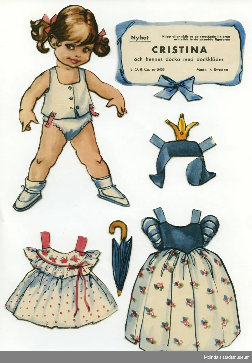Pappdocka med kläder och tillbehör från 1950-talet. Docka och kläder är märkta "Cristina" på baksidan - dockans namn. Dockan föreställer en flicka med brunt hår i tofsar, iklädd underkläder, strumpor och skor. Garderoben består av fem klänningar, en prinsessklänning med tillhörande huvudbonad, hängselbyxor, pyjamas, samt ytterkläder. I materialet ingår även tillbehör, såsom paraply, hårborste, blomsterkorg, väska och dockvagn. Pappdockan har dessutom en docka med egna kläder och tillbehör (MM 04662). På en liten skylt av papp står det: "Cristina och hennes docka med dockkläder, E. O. & Co. nr 5455, Made in Sweden". Texten är inramad av blått band och rosett. Docka och kläder förvaras i ett brunt kuvert, ursprungligen från Uppbördesverket, Göteborg (Skatteverket).