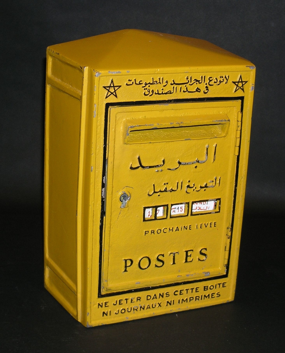Brevlåda i gul järnplåt med arabisk och fransk text- Tömningslucka framtill med från insidan omställbara tömningstider. Brevinläggsöppning utan fällbar lucka, låst med från insidan nedfällbar klaff. Den arabiska texten ovanför iläggsluckan flankeras av femuddiga stjärnor.
