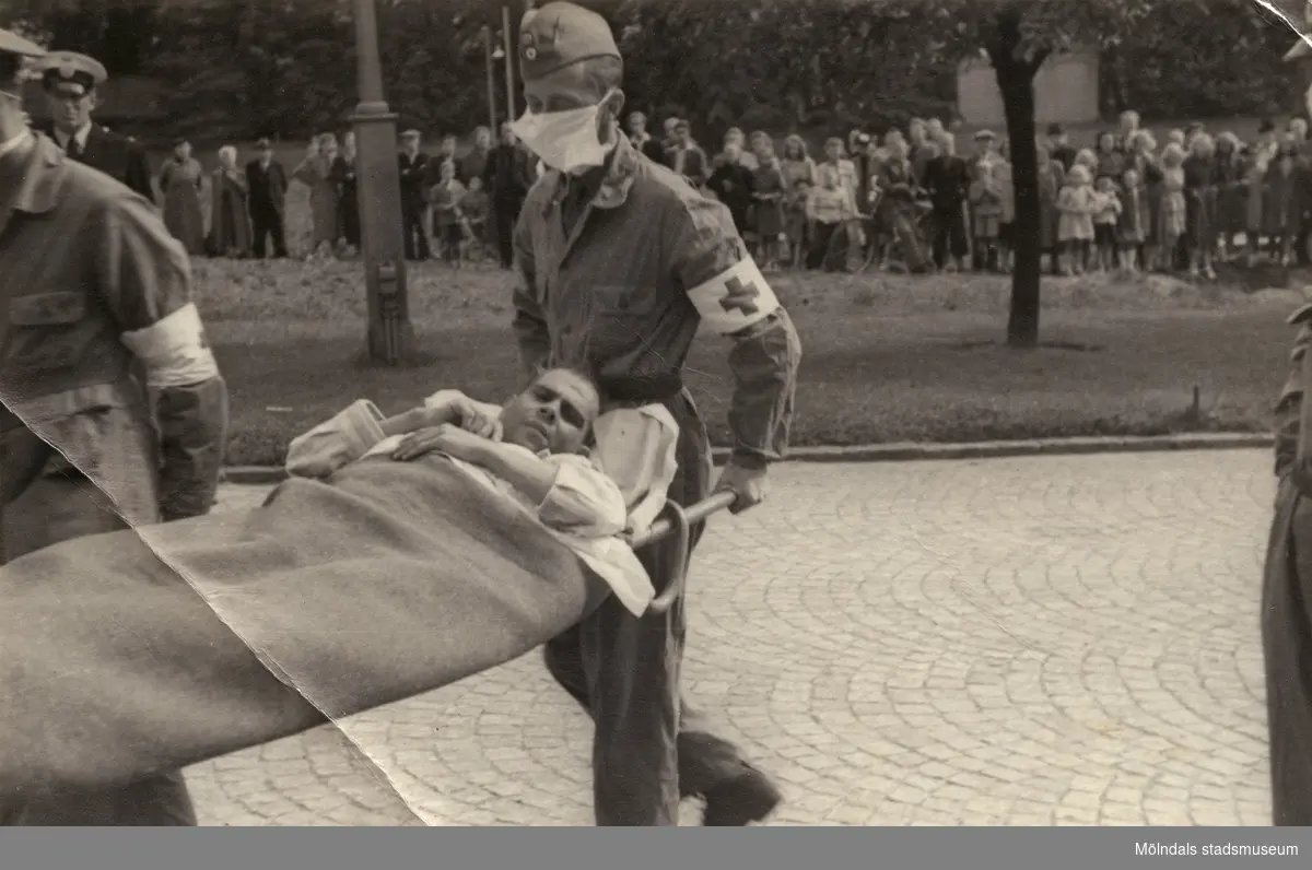"Karantänsförläggning" på Kvarnbyskolan för överlevande från koncentrationsläger i Tyskland och Polen 1945.  
Skolan fungerade under denna sommar som beredsskapssjukhus.

Manlig flykting blir buren på bår av Röda Korsets personal.