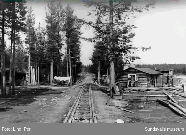 Alby 1898. Till vänster och höger i bild arbetarbostäder i mitten av bilden ett spår. Till höger två kvinnor.