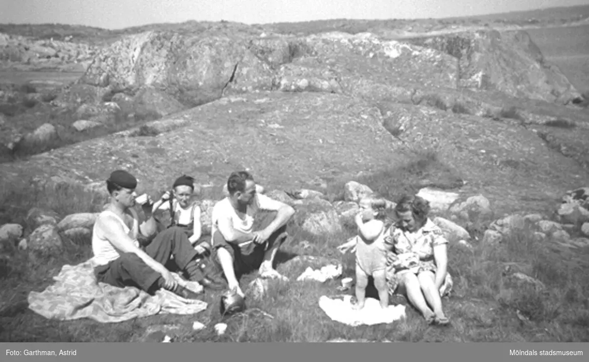 Helmer Garthman och sonen Leif samt Egron Andersson med sonen Lars och hustrun Gurli, 1950-tal. Dessa var grannar på Lerbrännargatan 1C i Mölndal. De var även grannar på Barnhemsgatan 21. De sitter på en gräsyta mellan Näsets klippor och fikar.