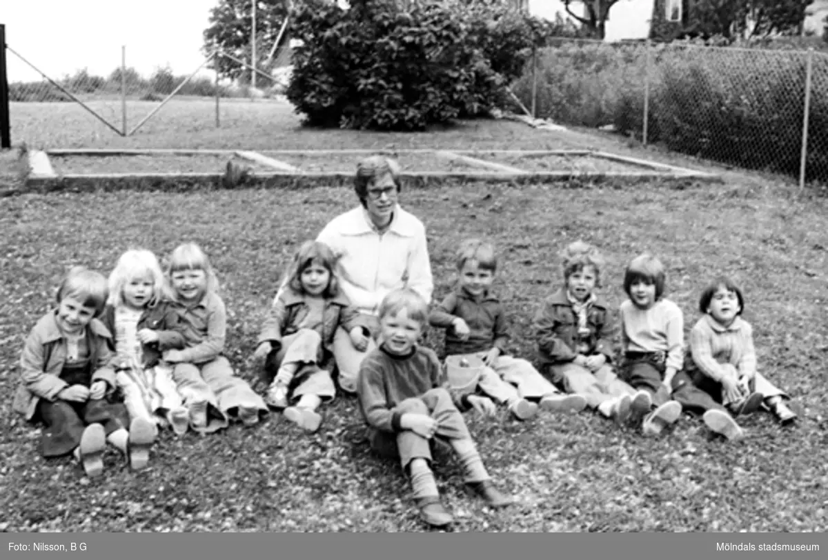Några barn och en fröken sitter i gräset. Holtermanska daghemmet 1973.