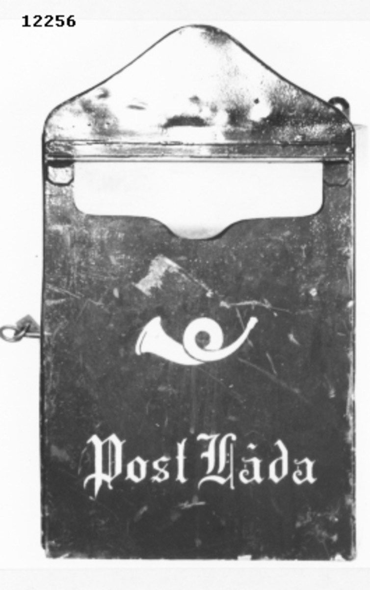 Postlåda av plåt med lås och nycklar samt beslag av mässing. På framsidan ett horn, målat i gult. Märkning: Postlåda (i gult).