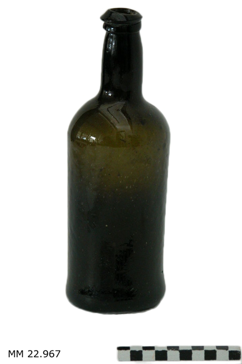 Flaska, sjöfynd från Nya Riga. En flaska i mörkgrönt glas med gott om blåsor i glaset. Botten är konkav (Kinnekullebotten, som i moderna flaskor för mousserande vin). Halsen formad med dubbla valkar i toppen. Korken murken men på plats. Flaskan är tom.