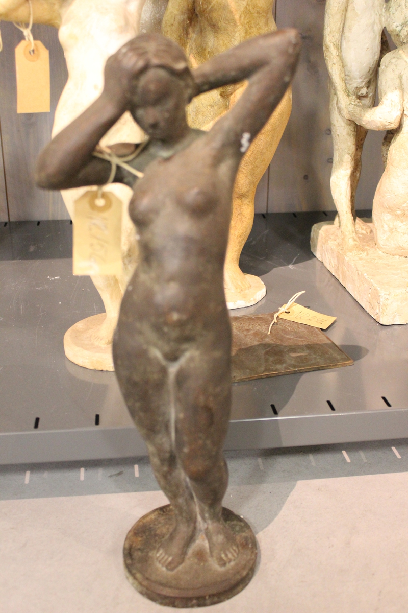 Skulptur i bronse av en kvinne som steller/ sveiper sitt hår.