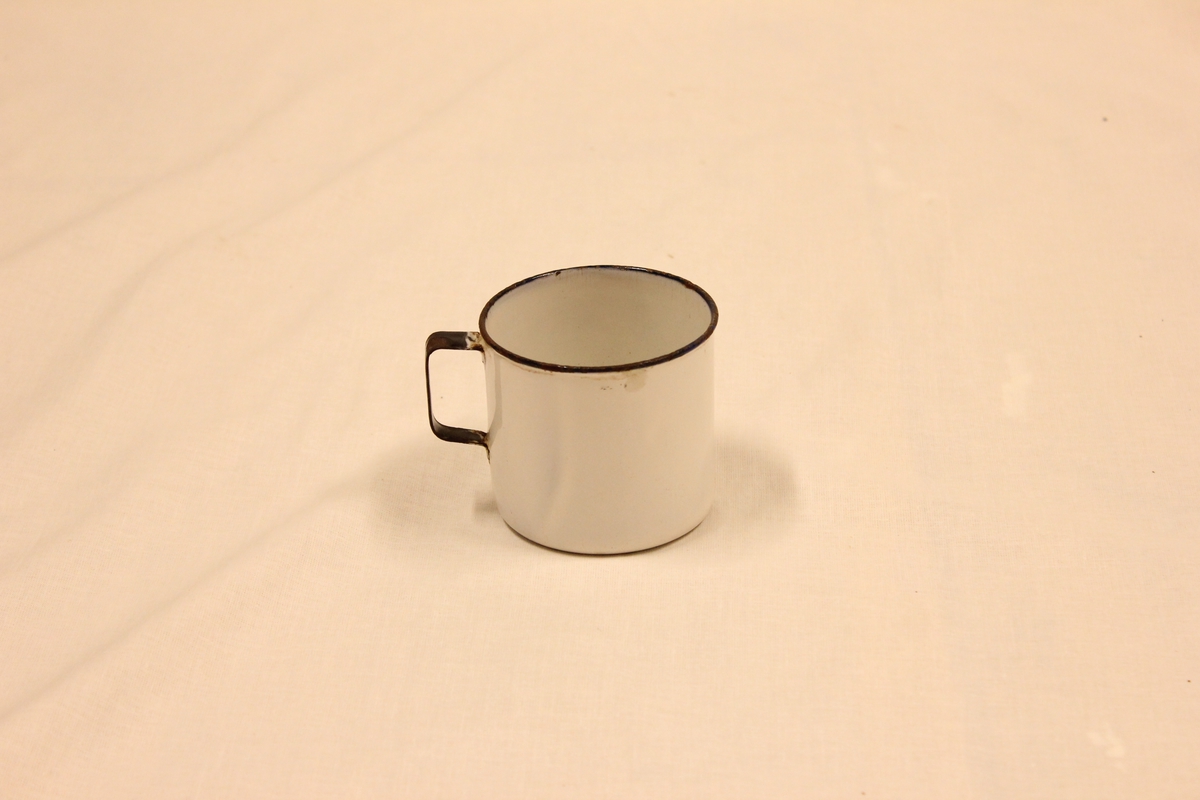 Hvitt blikk kopp med sort markering på håndtak og rundt åpningen oppe.