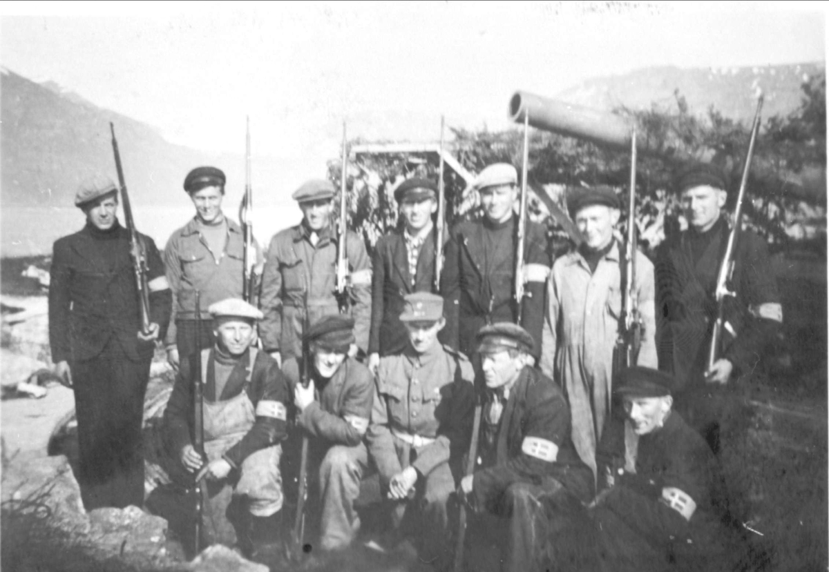 Gruppebilde av Bessebostad Skytterlag på vakt ved Ytre Elgsnes under frigjøringen. I bakgrunnen en kamuflert kanonstilling.