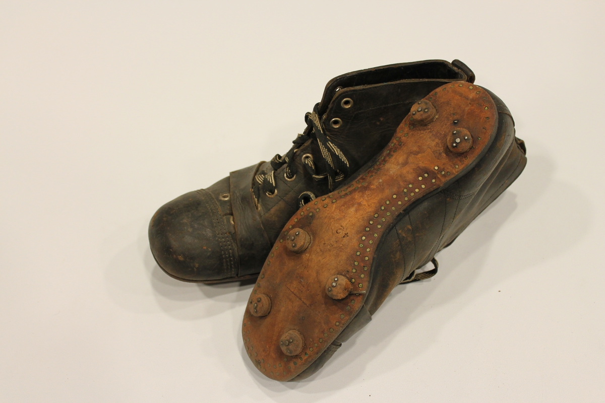 Fotballstøvler med jerntupp, påspikrede knotter og reim. Rødt pyntemerke på siden av begge støvlene. Størrelse 42