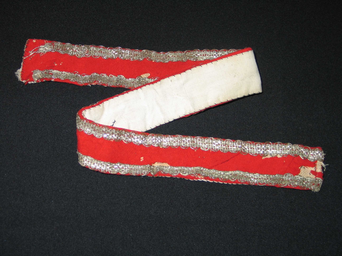 Raudt ullstoff på strie med to kantband i fletta metallband