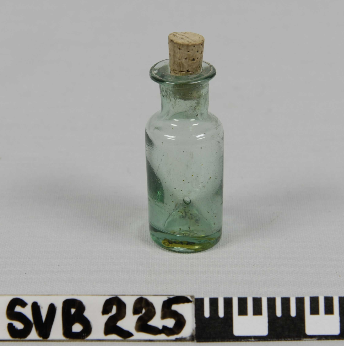 Miniatyrflaske i grønt glass med kjegleformet kork av korktre. Tydelige luftbobler i glasset. 