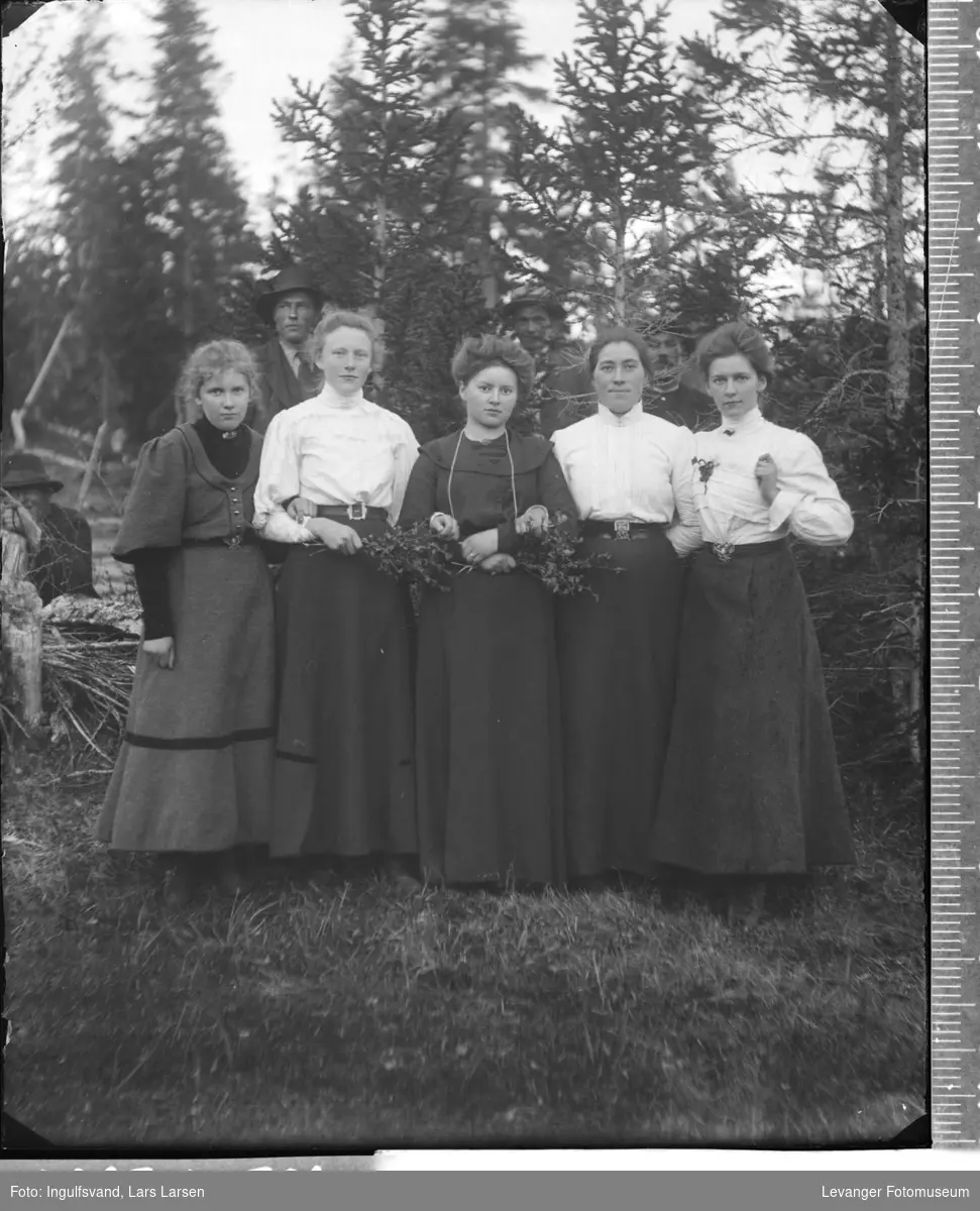 Gruppebilde av fem kvinner, med tre menn i bakgrunnen.