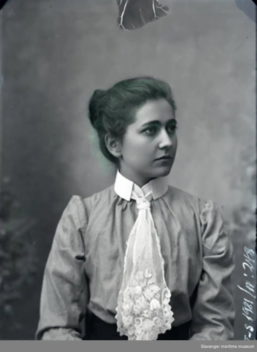 Portrett av ung kvinne med oppsatt hår og hvit silkebluse. Lett puff ved skuldrene. Blondesjal er knyttet rundt halsen med slipsknute. Nøytral bakgrunn. Samme som 1981-011-0299.