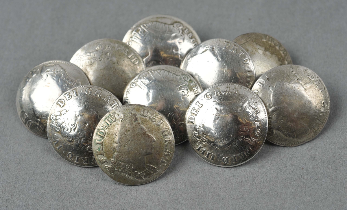 10 myntknappar. Myntar som er gjort kuvne og pålodda koparhempe. Myntane er dansk-norske 8-skillingsmyntar frå åra 1700-1729.
