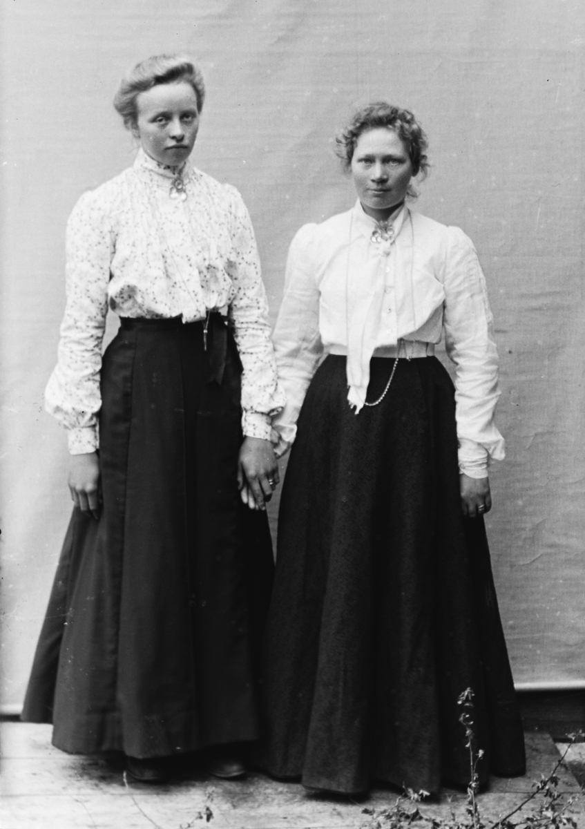 To stående kvinner i helfigur, holder hverandre i hendene, foran lerret. Gjertrud Lo (f. Høverstad) til venstre, kvinnen til høyre ikke navngitt