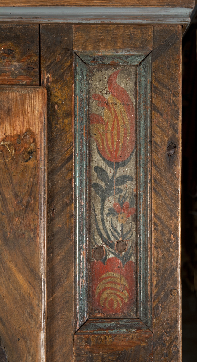 Bemålat skåp av trä, rak form. Fronten ådringsmålad i bruna nyanser. Dörr med gångjärn, beslag, lås och nyckel i järn (UM31019b). Övre delen av dörren har vit text: Ao 1790 JES, resterande initialer är oläsliga. Dörrspegel och totalt fyra sidospeglar dekorerade med stiliserade tulpaner (flammande tulpaner) i grönt, rött och gult mot vit botten. Det nytillverkade krönet är ådringsmålat i bruna nyanser, profileringar målade i två gråblå nyanser, en målad med rödaktig färg. Skåpets sidor och krönets ovansida har även de ådringsmålats med färg i bruna nyanser. Den nytillverkade lösa benställningen med hylla är ådringsmålad i bruna nyanser, de spiralvridna benen är svartmålade, liksom kulfötterna. Inredning: tre hyllor.
Benställningens mått: höjd 54 cm, bredd 110 cm, djup 53,5 cm.
Den ursprungliga målningen är sliten, framför allt på dörrens högra hörn.