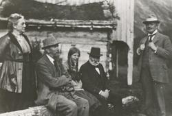 Fem personer samlet foran et hus. Mann med skjegg identifise