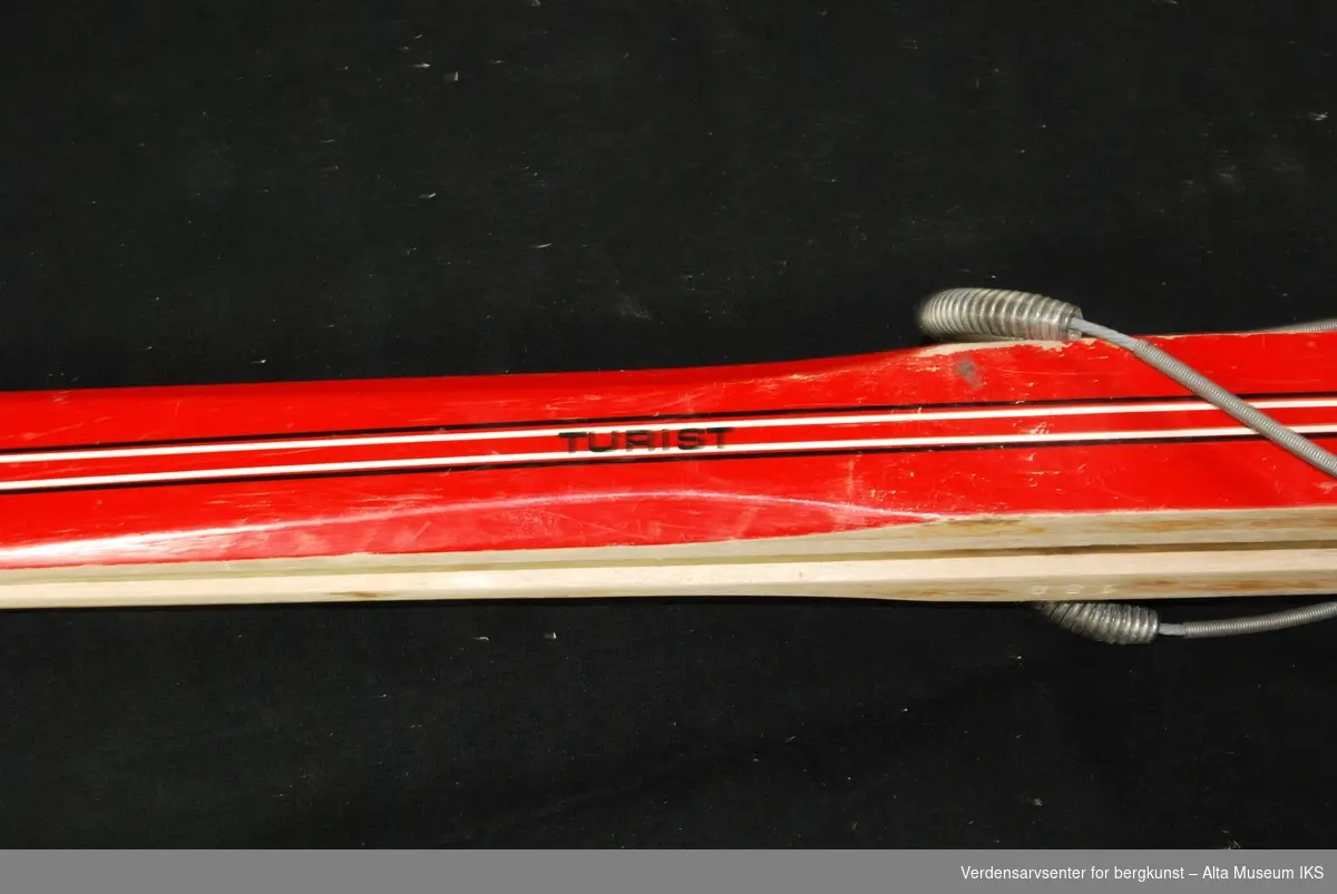 Røde laminerte ski, laget i Finland med norske bindinger. Stripete mønster.