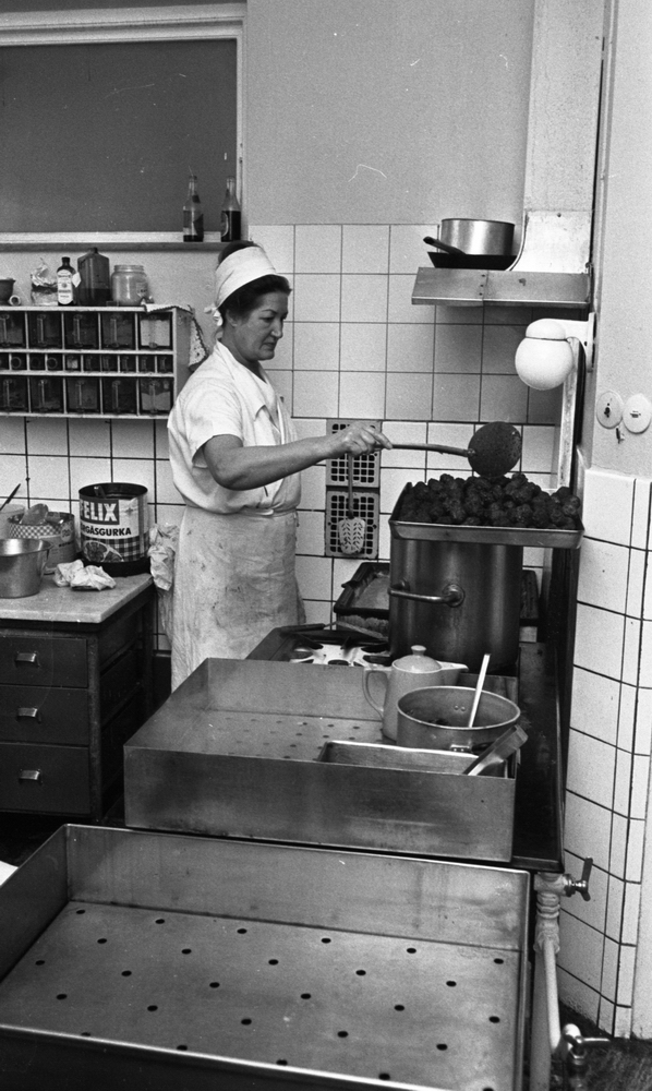 Fabriksmat, 9 mars 1966

En kokerska i vita arbetskläder är i färd med att sleva upp köttbullar i en ugnsform.
