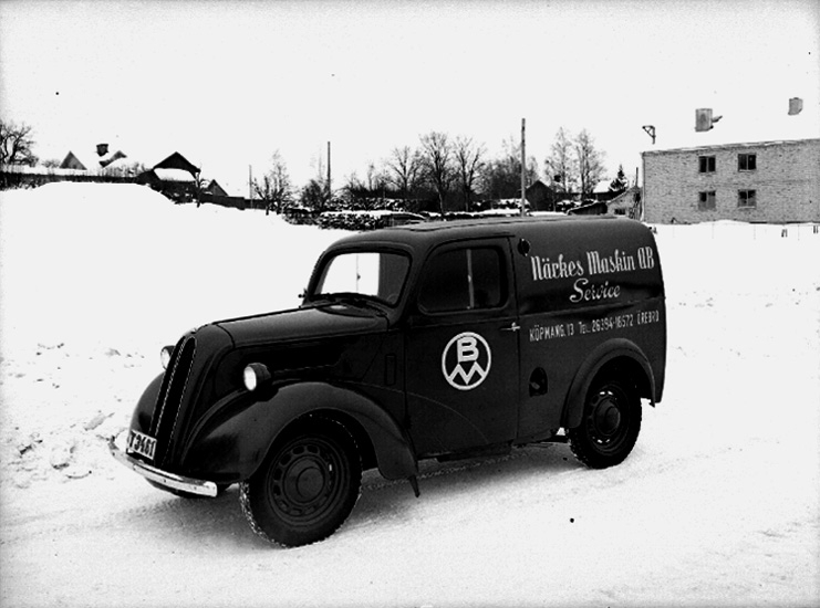 En bil.
Närkes Maskin AB, service, Köpmangatan 13, Örebro.
Bostadshus och byggnadder i bakgrunden.
Vintermotiv.
