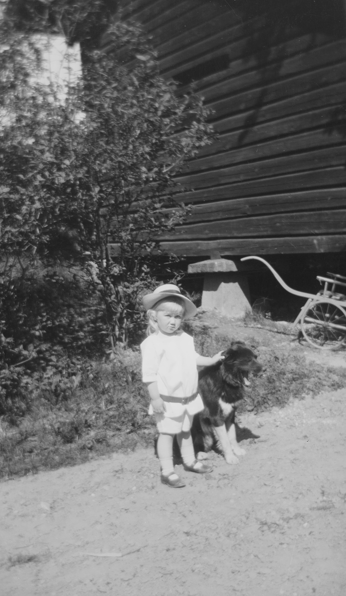 Iacob Ihlen Mathiesen står ved siden av en hund som gjesper ved et laftet hus.