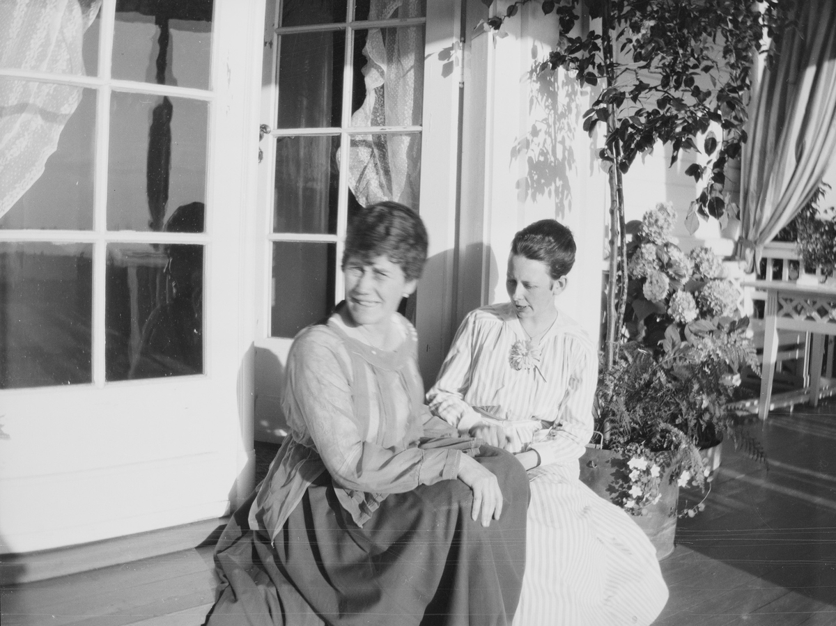Celina Ihlen Mathiesen og en annen kvinne sitter på et trappetrinn på den halvsirkelformede verandaen på Linderud Gård.