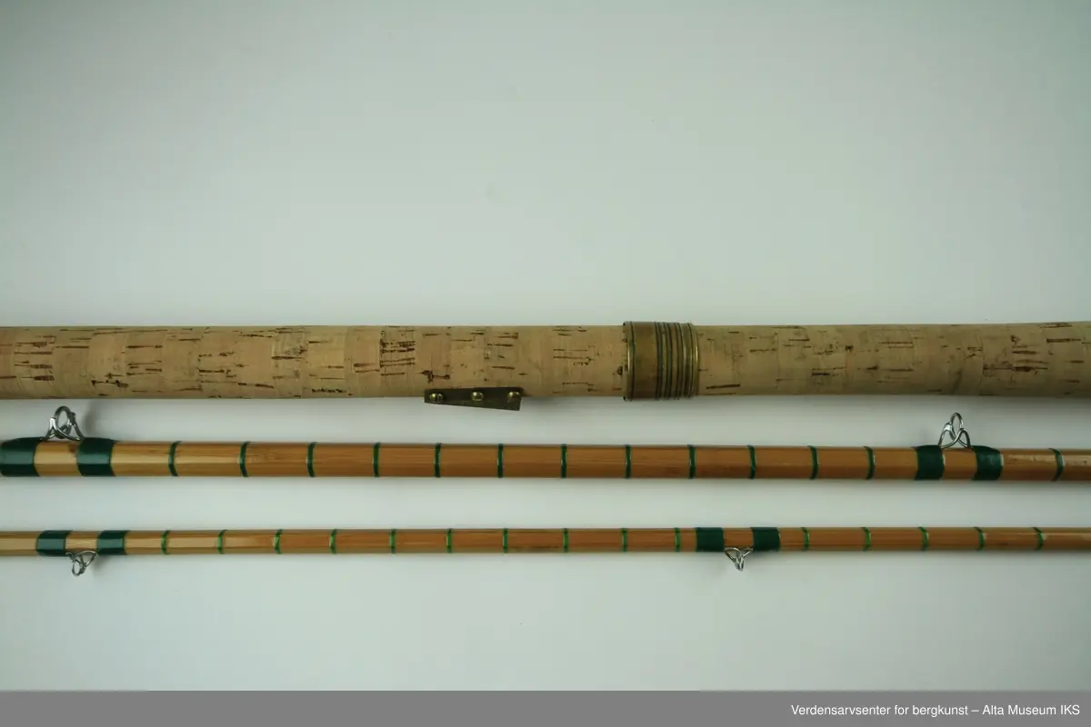 Tohånds fluestang. Tredelt. Tungbygd splitcane med stålkjerne. klasse # 11-12. Skruholker (kom etter knyteholkene) av messing. Sliding ring snellefeste. Har vært brukket i toppen mellom andre og tredje ring. Nye grønne surringer. Endebutt i messing og gummi.