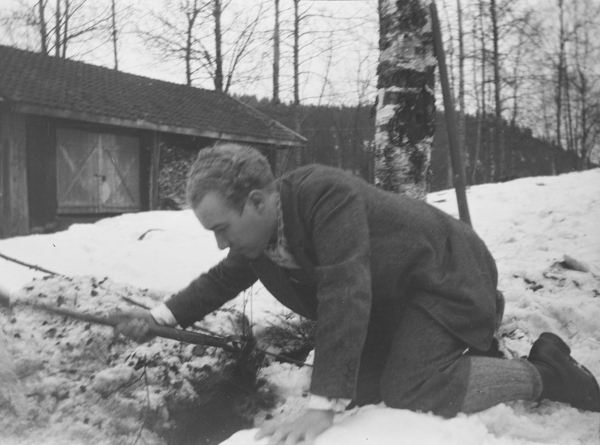Iacob Ihlen Mathiesen ligger på knærne i snøen og ser ut som han graver fram noe under snøen utenfor uthuset/ vedskjulet i Jeppedalen.