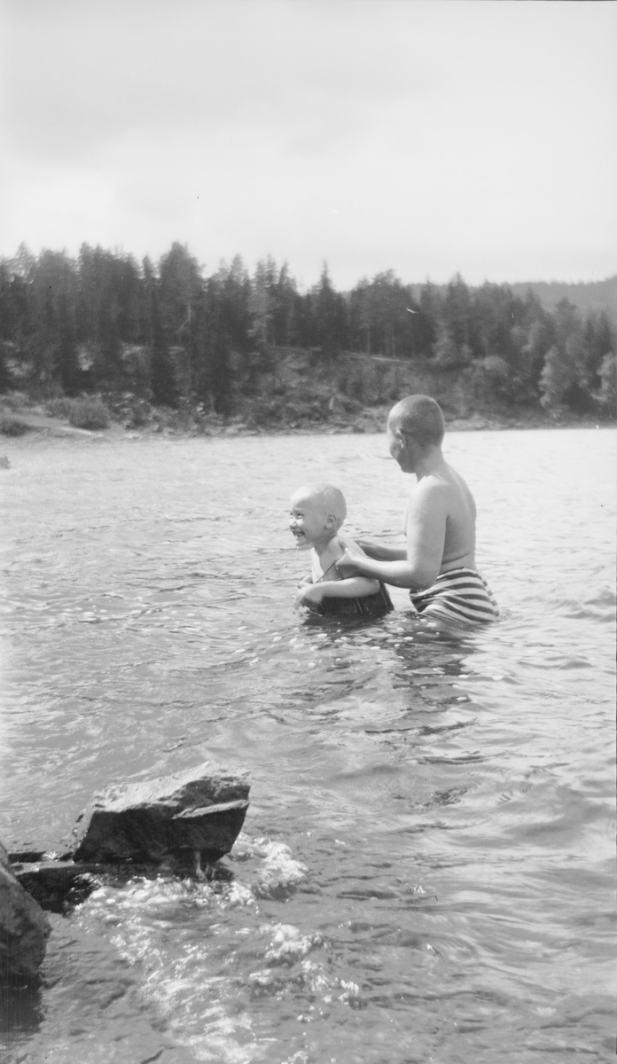 En eldre gutt hjelper en yngre gutt med svømmetrening i en innsjø på østlandet. Den yngste gutten har på svømmebelte.