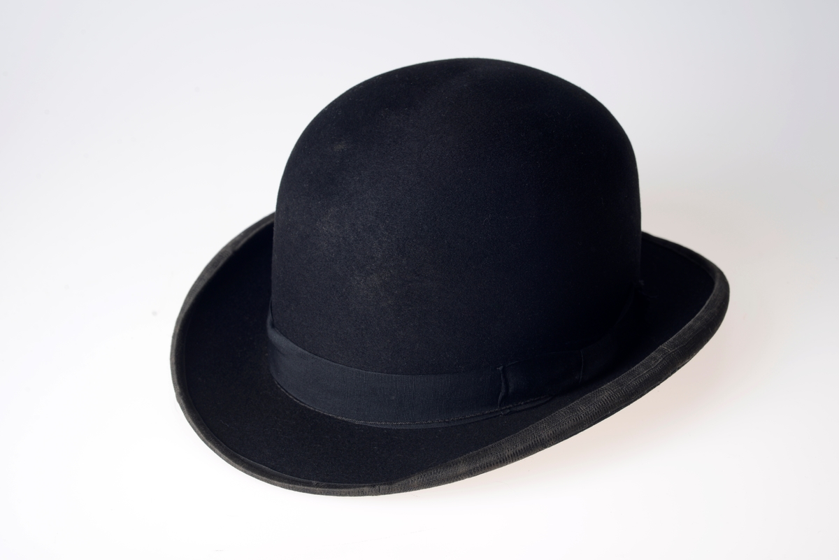 Stempel og firmanavn på silkestoffet inni hatten. Svettebånd av brunt lær. Sort bånd rundt pullen. Kanten på bremmen er kantet med et sort bånd.