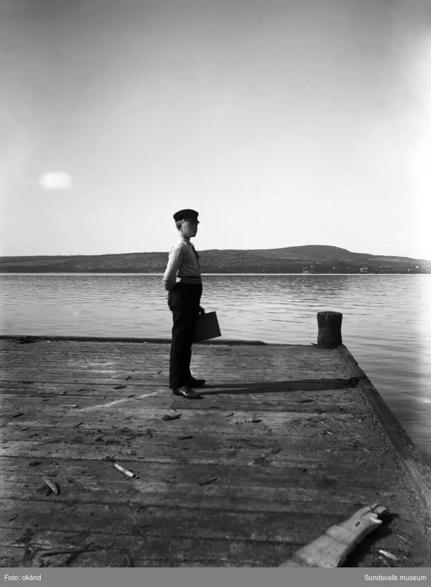 En pojke blickar ut från en båtbrygga. Troligen på Alnösidan eftersom man kan se över till Skönsmon och Villa Kumo på fastlandet i bakgrunden.