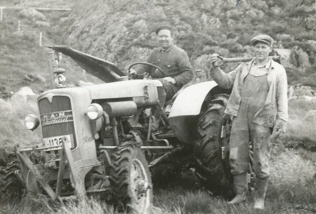 Eirik Håland (1924 - ) og Ommund Taksdal (1912) - 2004) grev veiter.
Ommund har rektignok spade på aksla men ein kan skimta slåmaskin på traktoren så det er lite truleg at det er montert graveutstyr i tillegg.