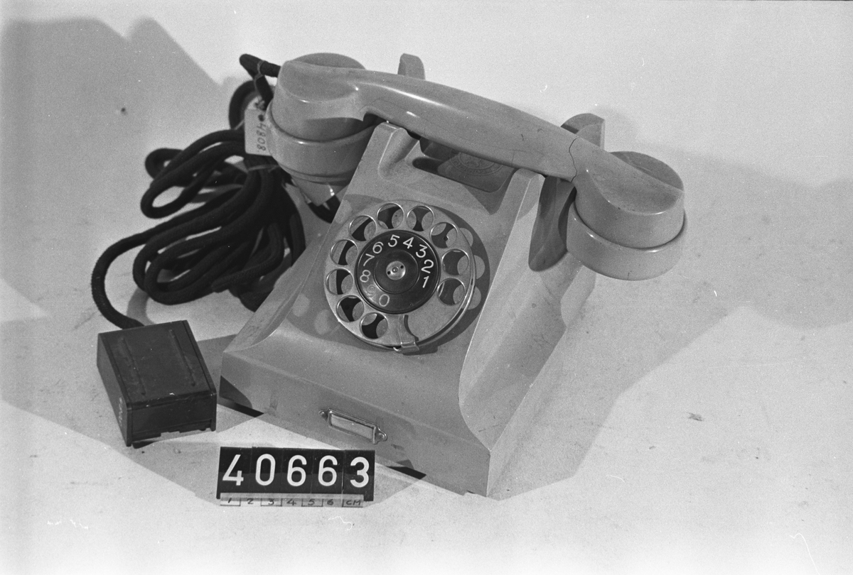 Telefonapparat BC 330, ändstationsapparat för AT-system. Bordapparat modell m33 av grå plast med fingerskiva av förnicklad mässing och textilklätt apparatsnöre anslutet till väggplint med lock av svartlackerad plåt. Märkt:4808.