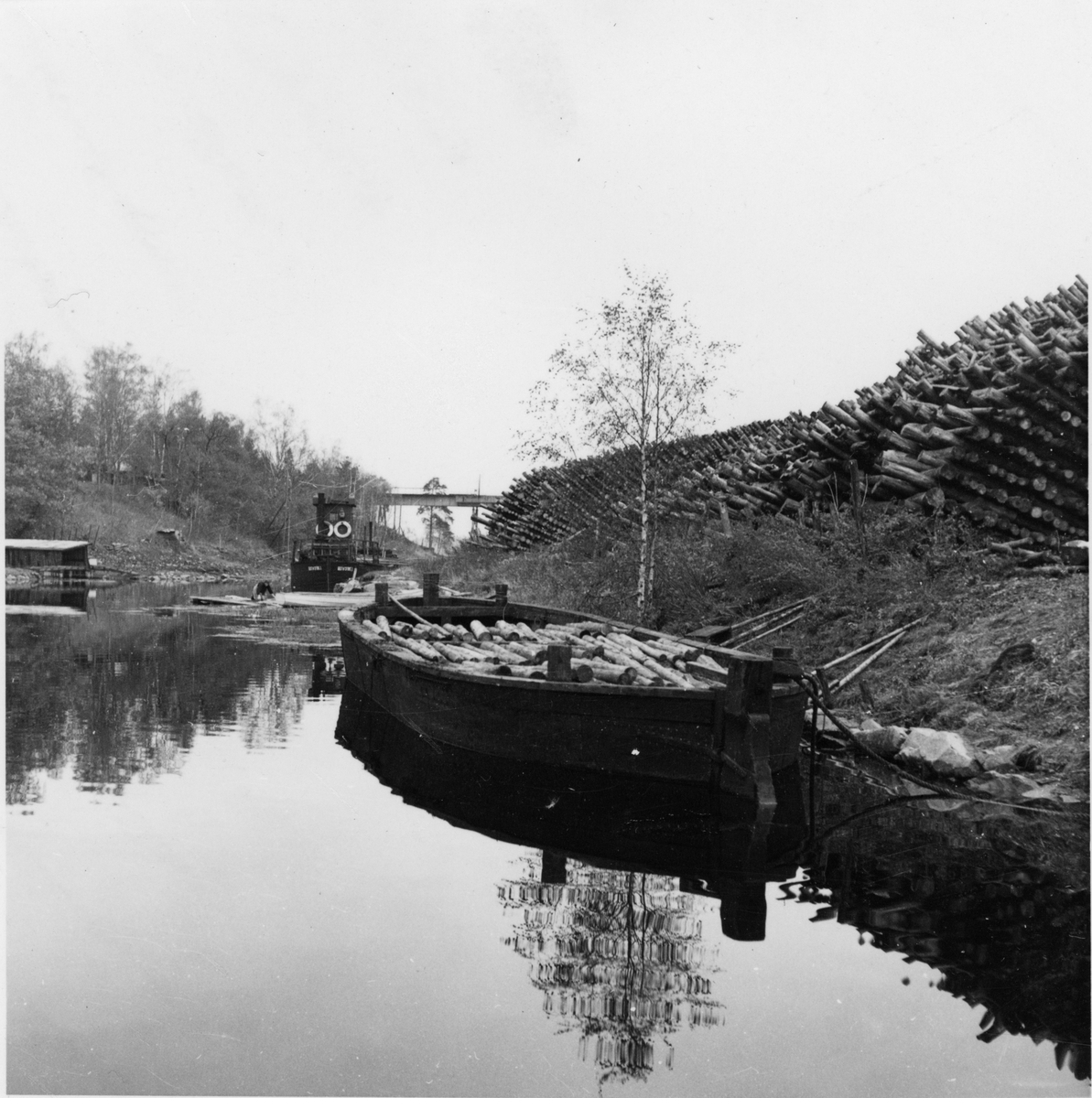 Sulfatfabrik. Gustafsfors Fabrikers Aktiebolag. Kanalen ovanför slussen. En vedpråm och en vedfärja. Järnvägsbron i bakgrunden och till höger vedupplag.