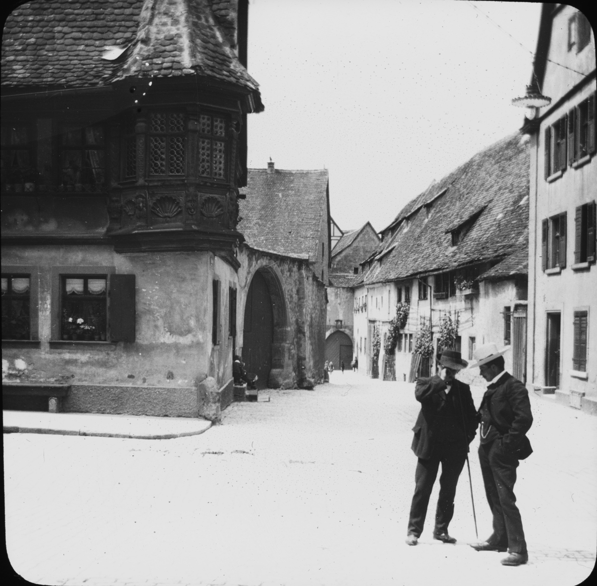 Skioptikonbild med motiv av två språkande män på gata, Klingen Strasse, i Rothenburg.
Bilden har förvarats i kartong märkt: Vårresan 1910. Rothenburg. XXX. Text på bild: " Klingen Strasse".