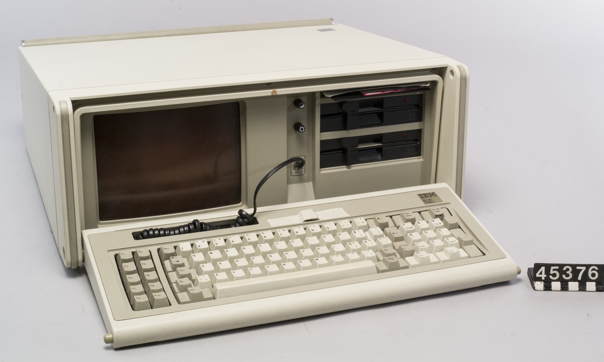 IBM 5155 Portable Personal Computer. Datorn har en inbyggd 5-tumsskärm, avtagbart tangentbord och två diskettenheter för 5 1/4 tumsdisketter. Datorn väger cirka 17 kg. I blixtlåsförsedd väska av tyg med axelrem, för transport.  I erbjudandet ingår förutom själva datorn även 2 disketter med operativsystem och dataspelet Decathlon  Ser nr 0079149-5155