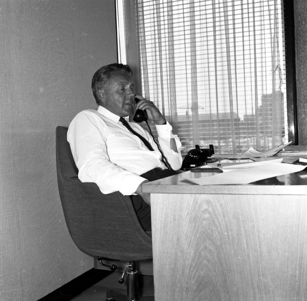 Landskap. En person ansatt i Braathens SAFE bak et skrivebord, fører en telefonsamtale.