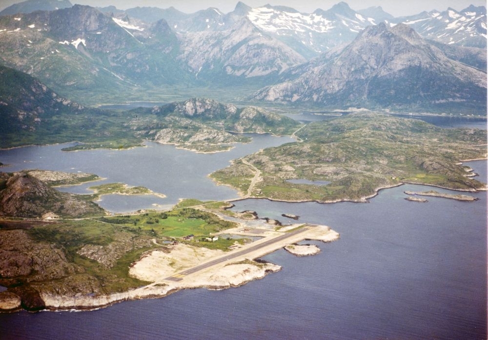 Lufthavn/Flyplass. Svolvær/Helle. Et fly passerer området og under oss ser vi flyplassen lokalisert i fjæra av Austnesfjorden.