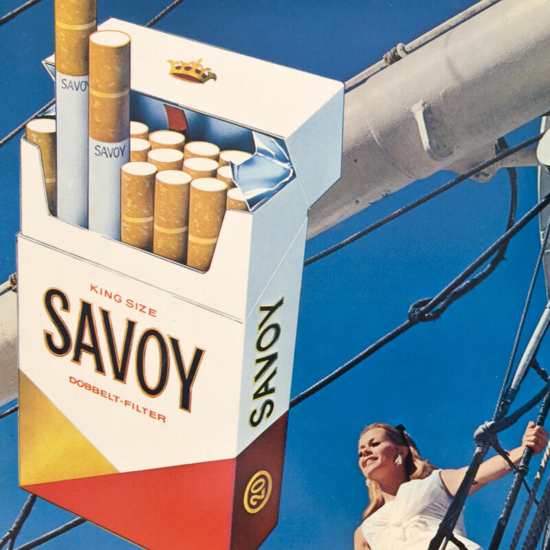 Reklameskilt. En pakke sigaretter i forgrunnen. En dame om bord på en båt i bakgrunnen (Foto/Photo)