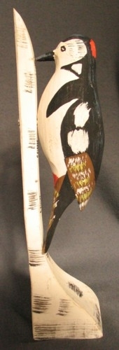Målad hackspett i trä. Fågeln är monterad på en björkstamsmålad pinne. Tillverkad av "Pinkatorparn" Sven Dal. 
Fåglarna målades av olika kvinnor på bygden.