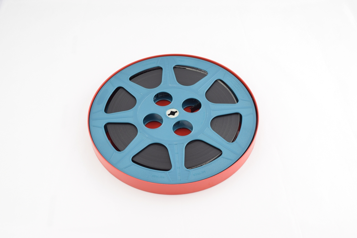 Filmrull i eske. Film på blå plastikkspole. Rødt rundt etui med rund grønn etikett.