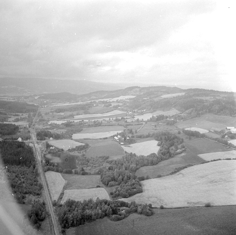 Flyfoto fra Ringsaker. Utsikt vestover Rudshøgda. Gården Simenstad i høyre bildekant, og Rud midt i bildet. Vegbrua over jernbanen er markert med blå sirkel her: