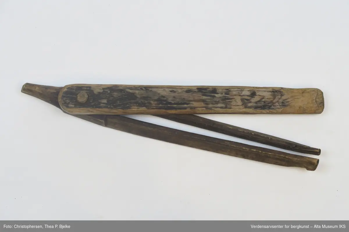 Avlang gaffel med dreibart lokk festet med en treplugg. Den ene enden er formet i en spiss. Basert på fargen ser treverket ut til å ha blitt tjærebehandlet.