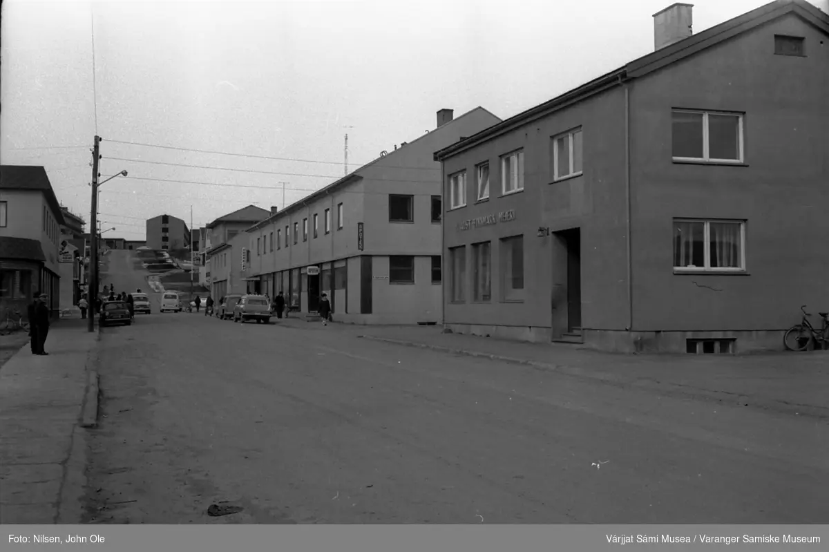 Gatebilde fra Vadsø sentrum, Bildet er tatt i Tollbugata. Statens hus i bakgrunnen. Apoteket til høyre som lå i Esbensenbygget den gang. Aust Finnmark Meieri helt til høyre. April 1967