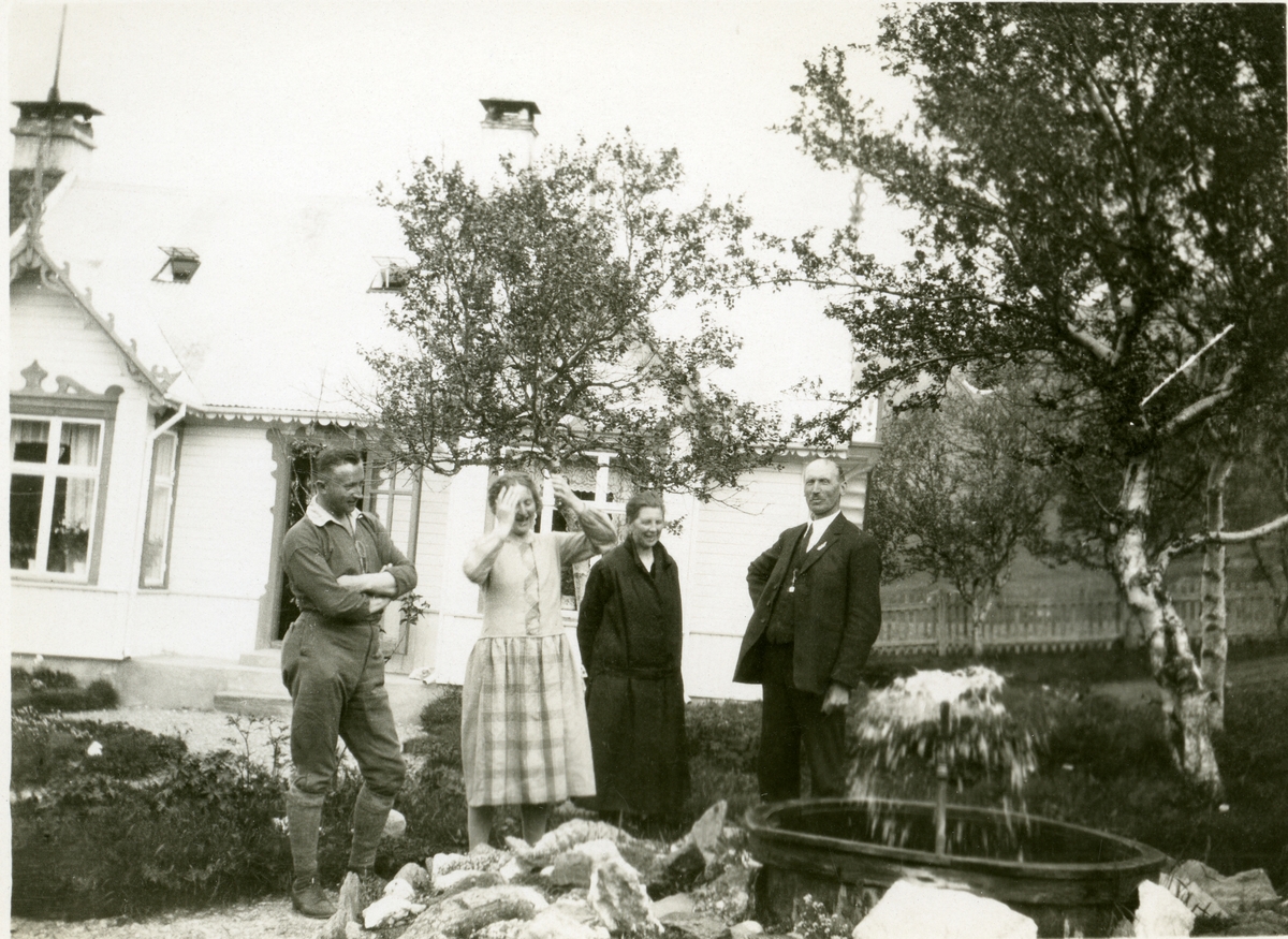 To kvinner og to menn avbildet ved en liten fontene, i en hage foran et bolighus. Mannen til høyre er Olaus Islandsmoen.
