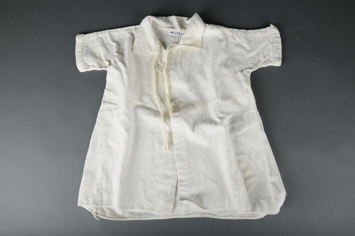 Hvit babykjortel med korte ermer og knytting ved kragen.