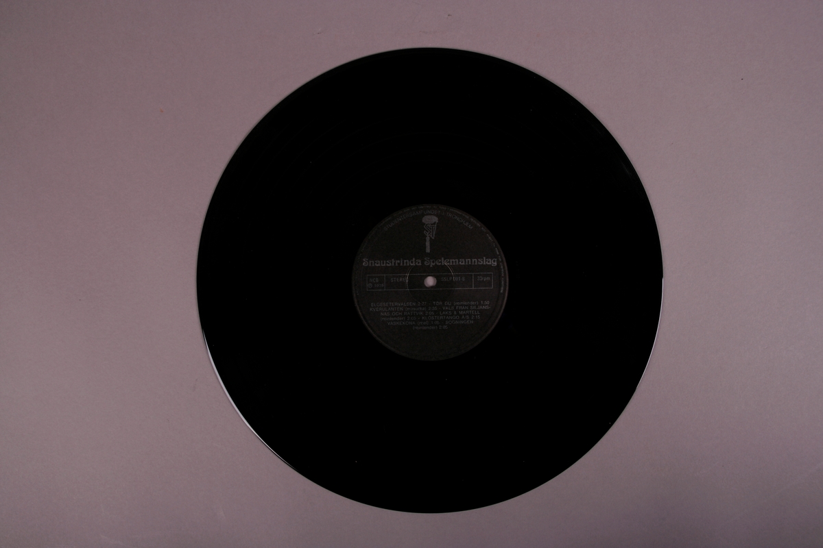 Grammofonplate i svart vinyl og plateomslag i papp, samt en plastlomme. Bilde på omslag viser Snaustrinda Spelemannslag.